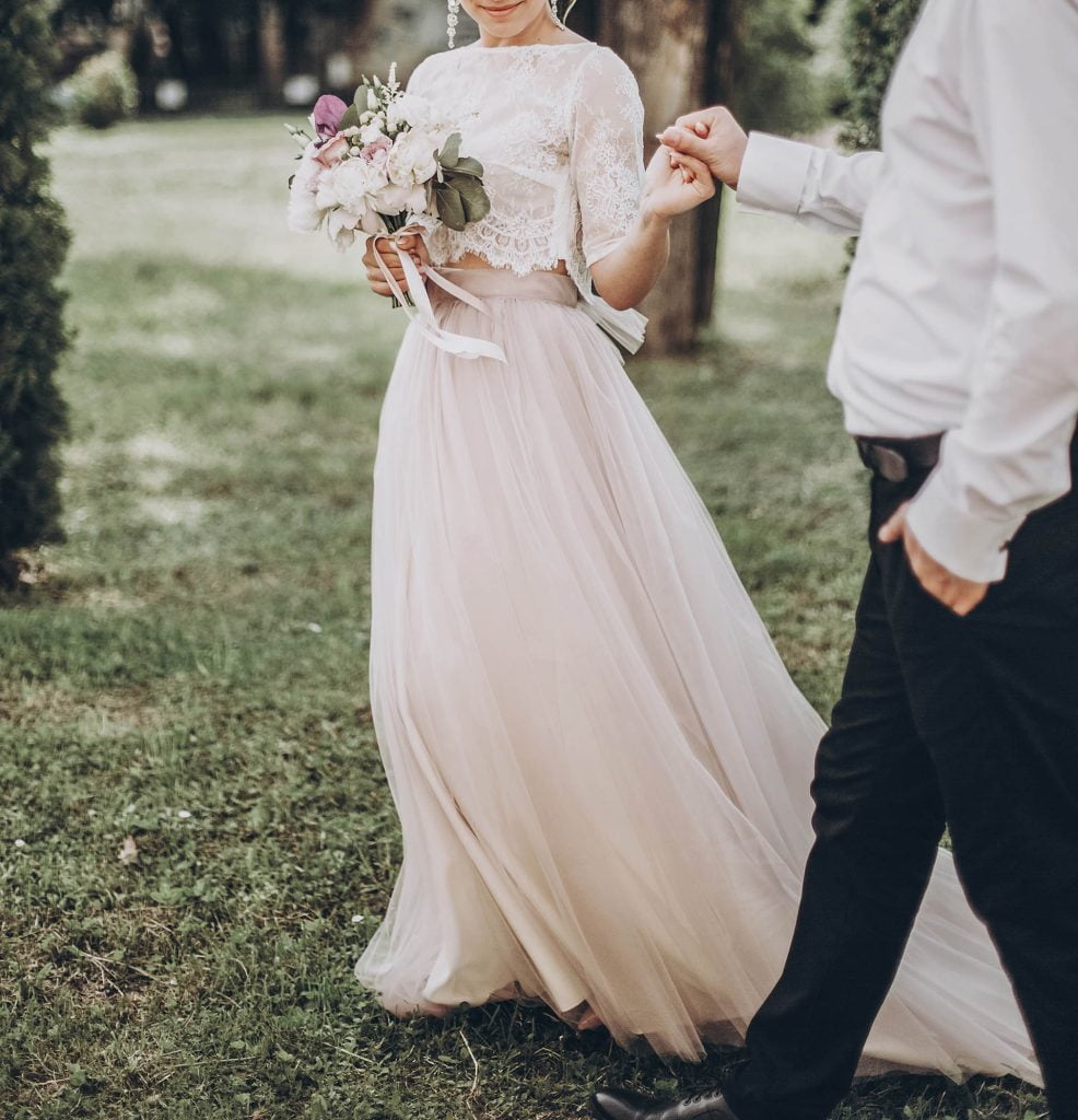 stylish wedding bride and groom walking in sunny park holding ha