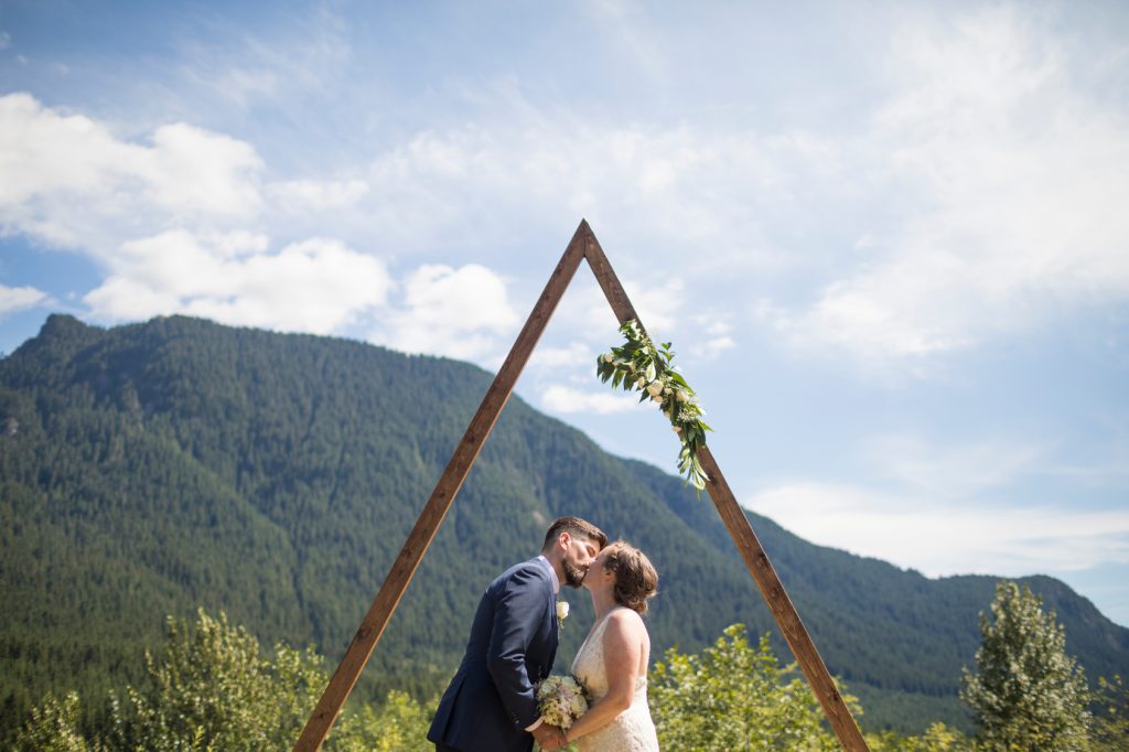 side view of newlywed couple kissing while standing against mountain at wedding ceremony