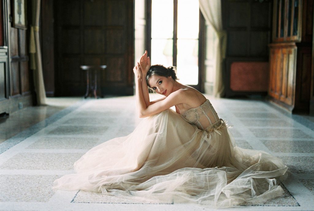 bride sits on the floor in front of the window of an old villa