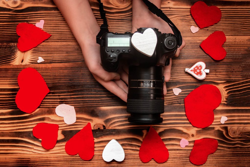 gift for valentine's day for photographer. camera in hands onwooden background. handmade hearts from felt.