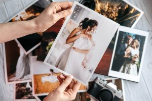 printed wedding photos with the bride and groom, a vintage black camera and woman hands with photo